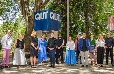 QUT staff standing in front of QUT plith logo